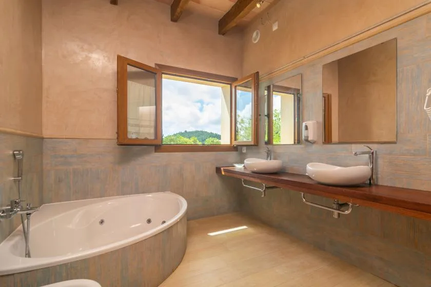 Un baño con una bañera grande y una encimera de madera bajo ventanas abiertas.