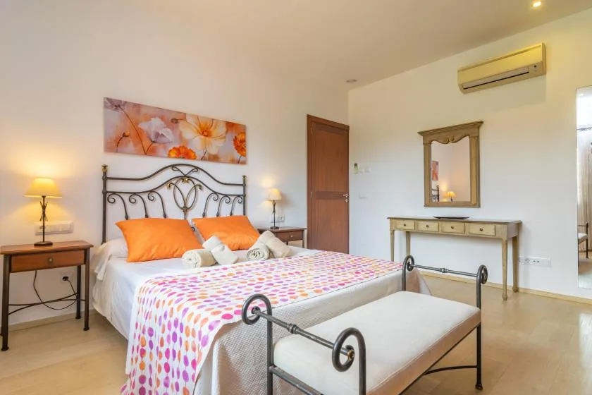 Un dormitorio con cama de metal, ropa de cama colorida, mesillas y un tocador.