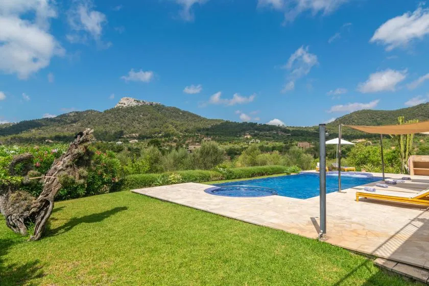 Una piscina y un patio pavimentado están junto a un césped verde, con colinas al fondo.