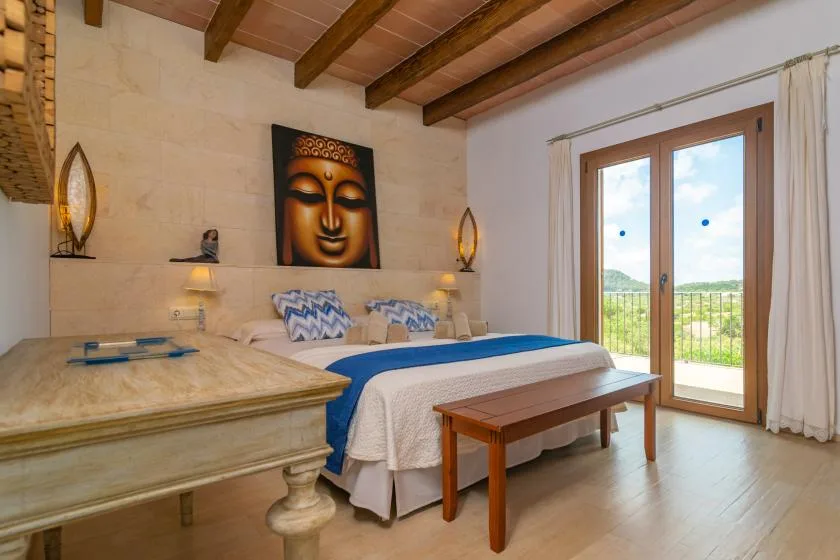 Un dormitorio con una cama bajo una pintura de Buda y puertas de cristal que dan a un balcón.