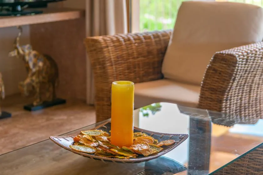 Una zona de estar con una mesa de vidrio y una vela amarilla alta.