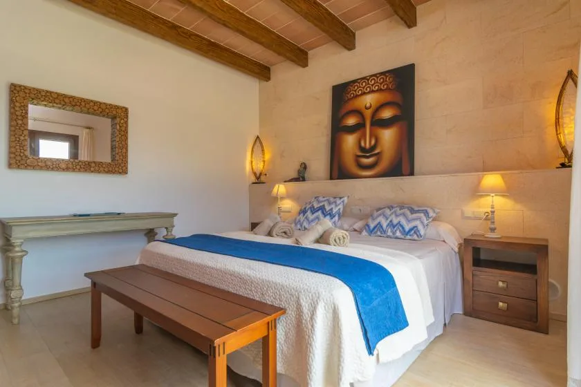 Un dormitorio con una cama vestida con ropa de cama blanca y azul bajo un retrato de Buda.