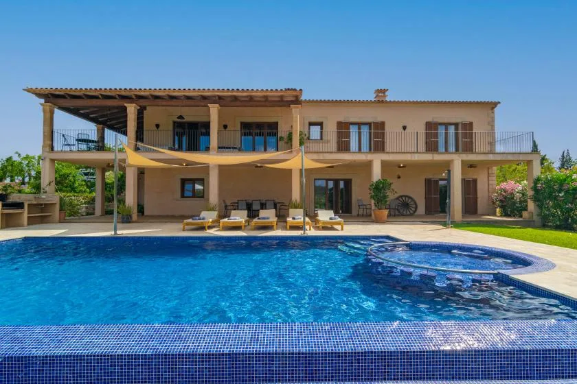 Una amplia piscina al aire libre está frente a una casa de dos plantas.