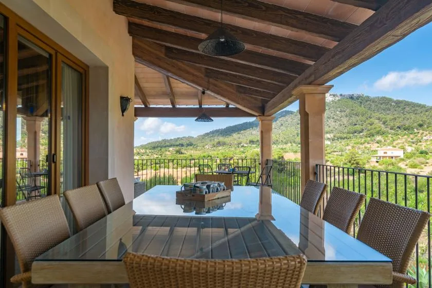Un comedor exterior cubierto tiene una mesa de vidrio y vistas a colinas verdes.