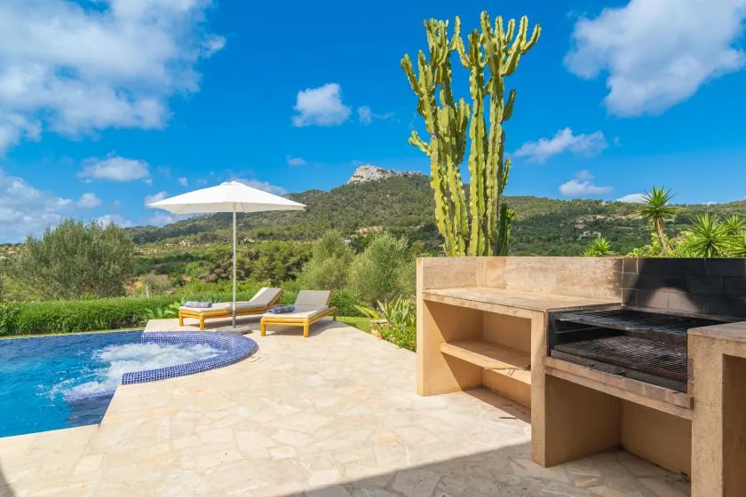 Un patio junto a la piscina con asientos, una sombrilla y una parrilla al aire libre.