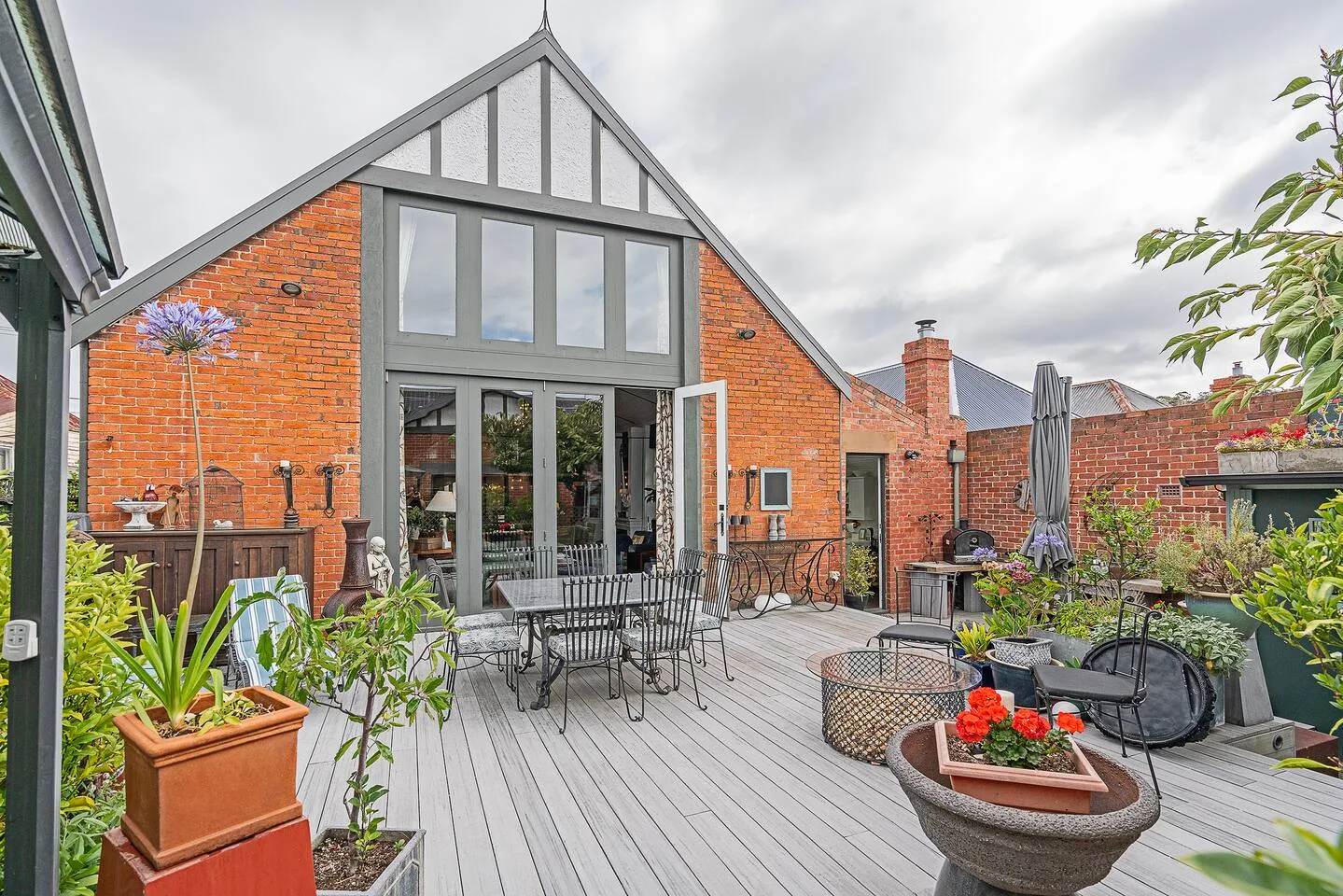 Un patio exterior con una mesa de comedor, asientos, plantas en macetas y una casa de ladrillo.