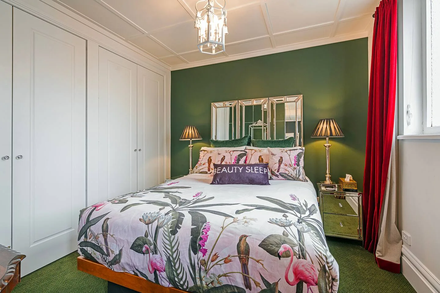Un dormitorio con ropa de cama floral, armarios empotrados blancos y una pared verde.