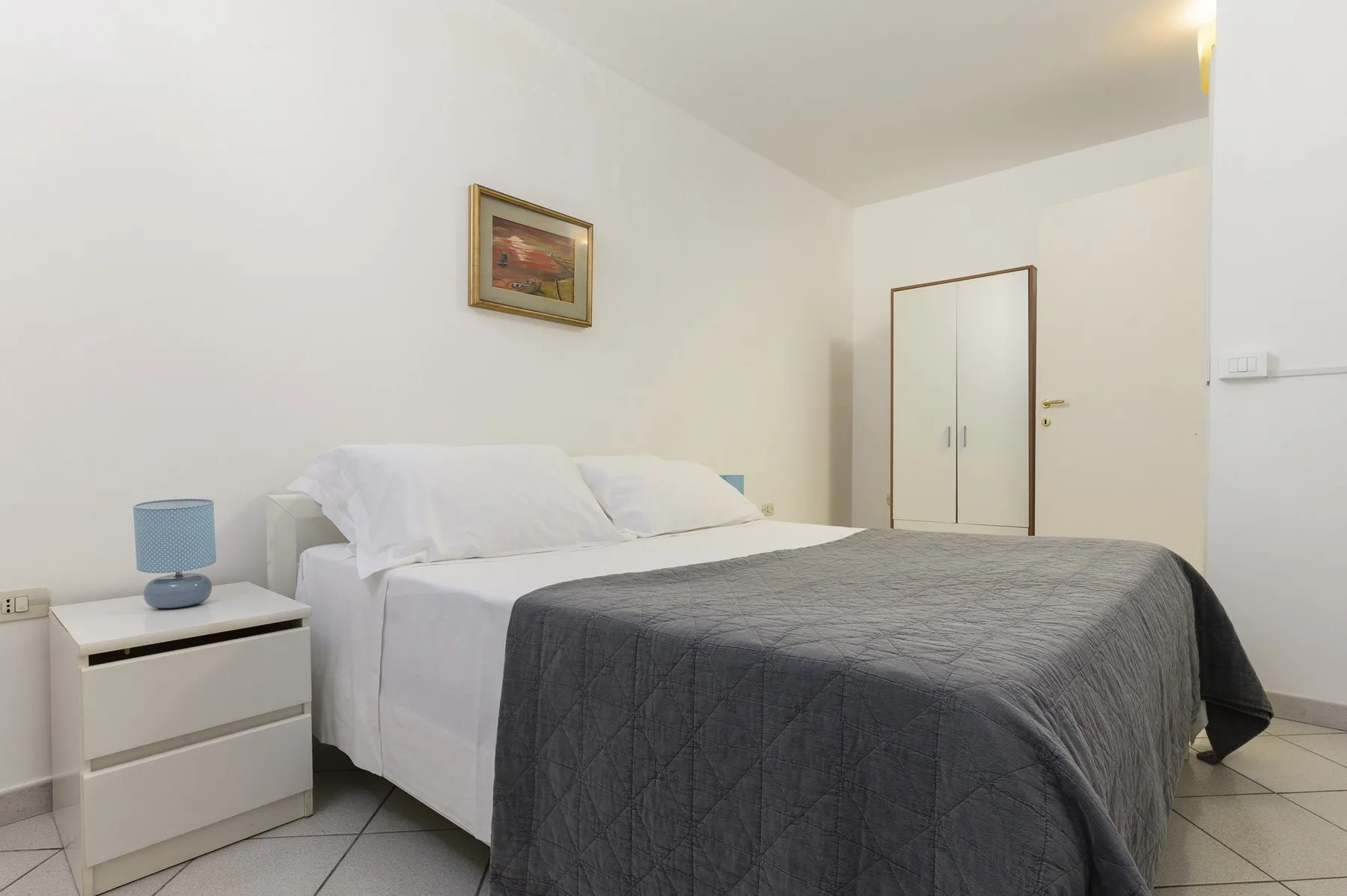 A bedroom with a bed covered by a gray blanket and a bedside table.