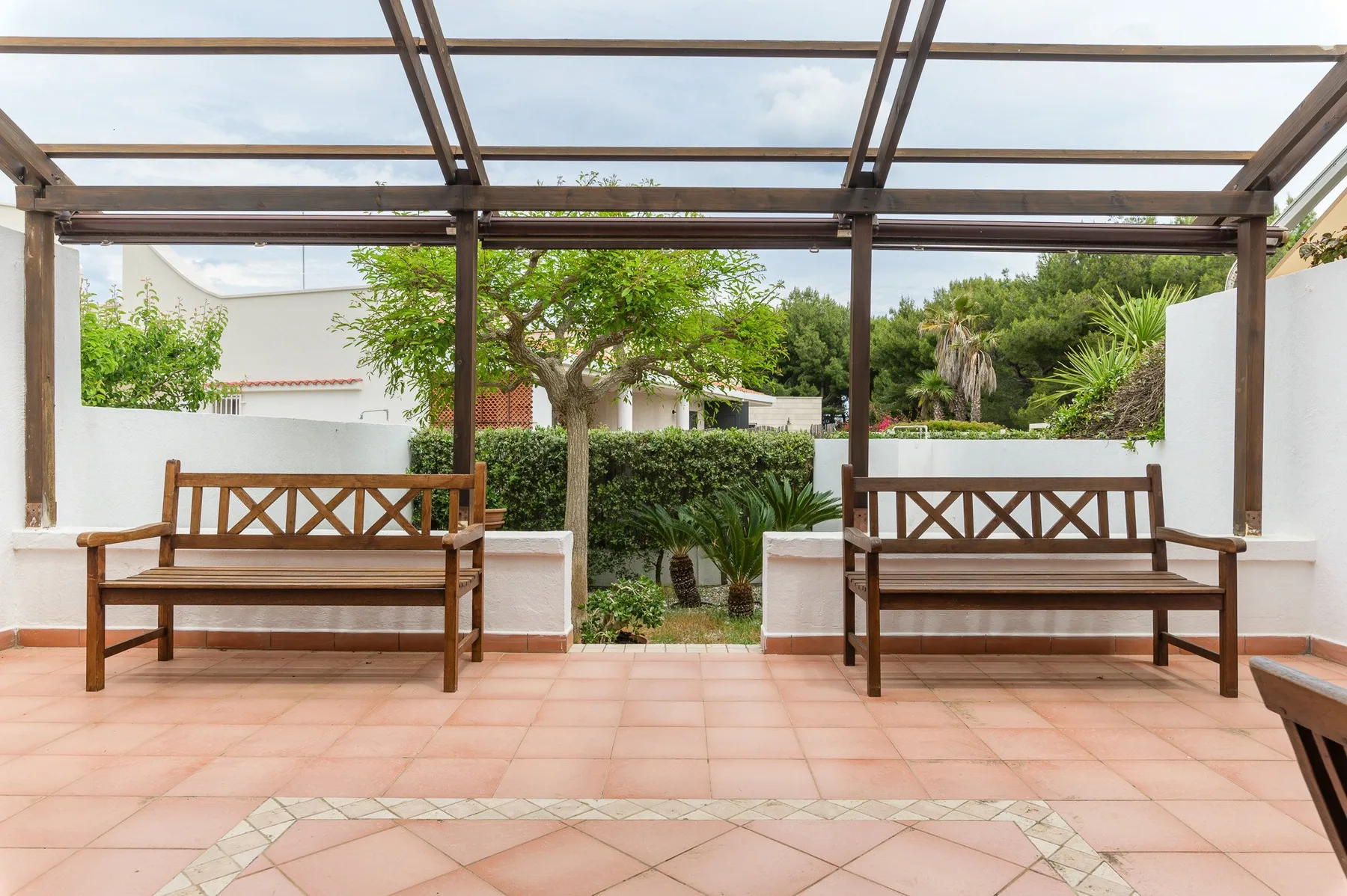 A tiled outdoor patio with wooden benches beneath a pergola.