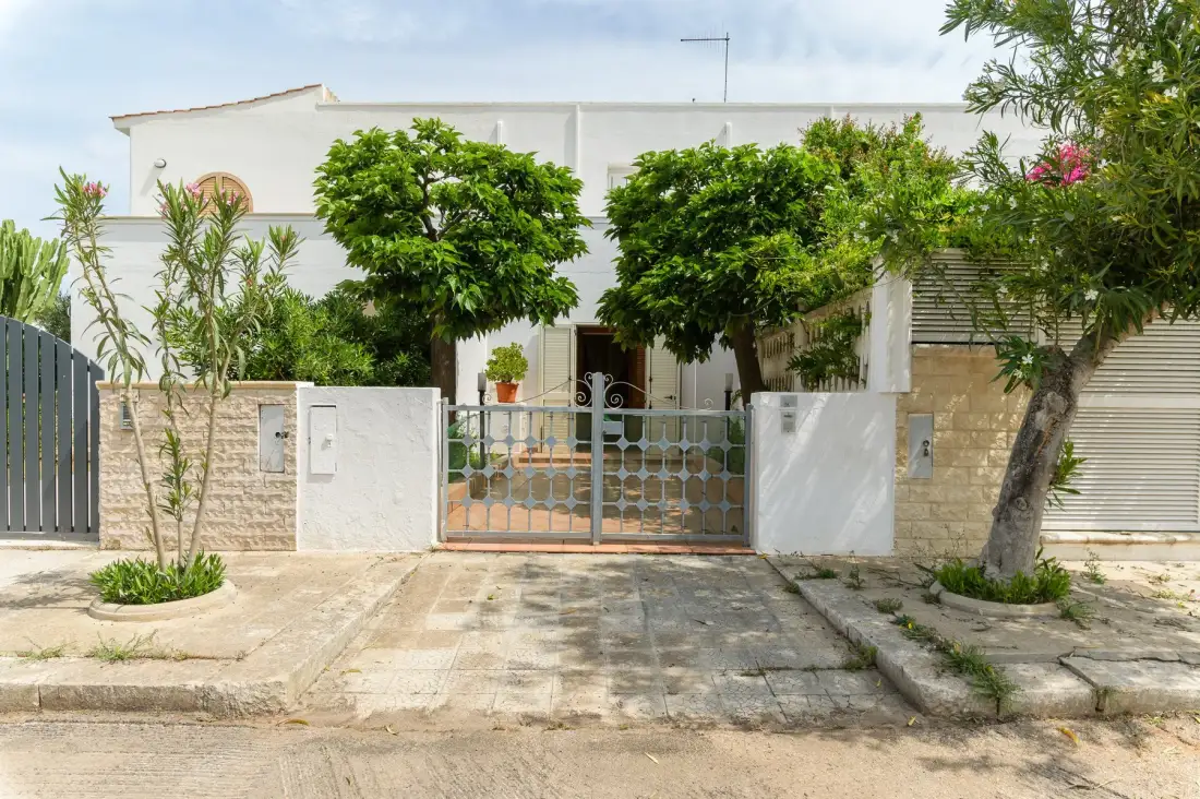 A gated building entrance is framed by leafy trees and low white walls.
