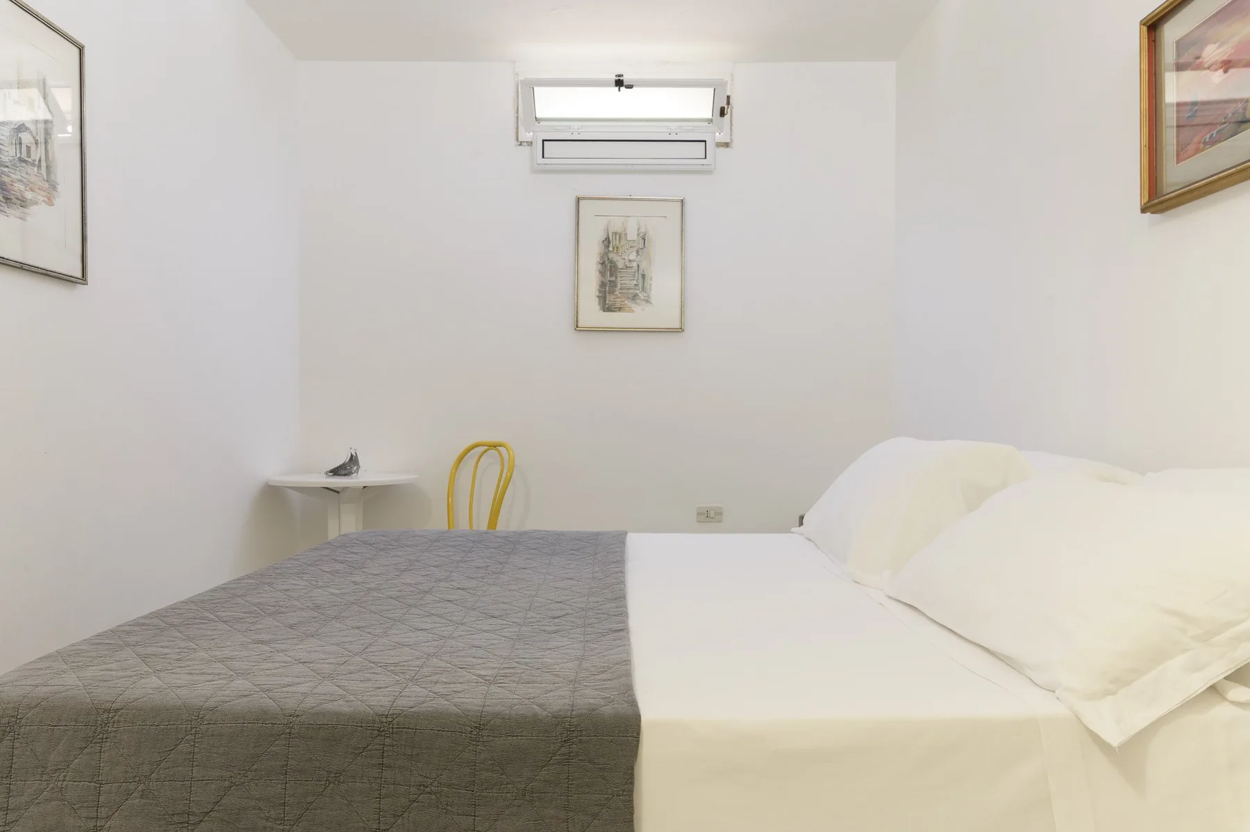 A bedroom with a bed covered in white bedding and a gray blanket.