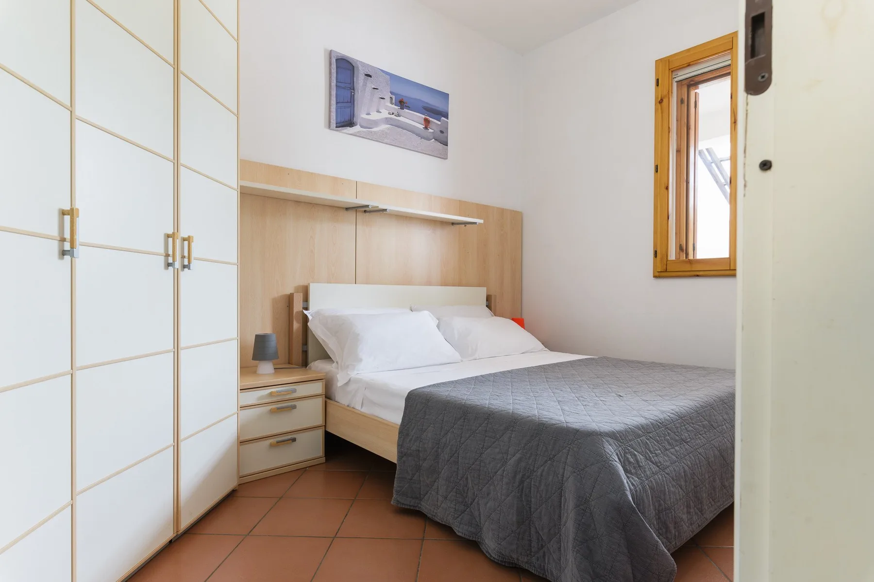 A bedroom with a bed, built-in wardrobes, and a small window.