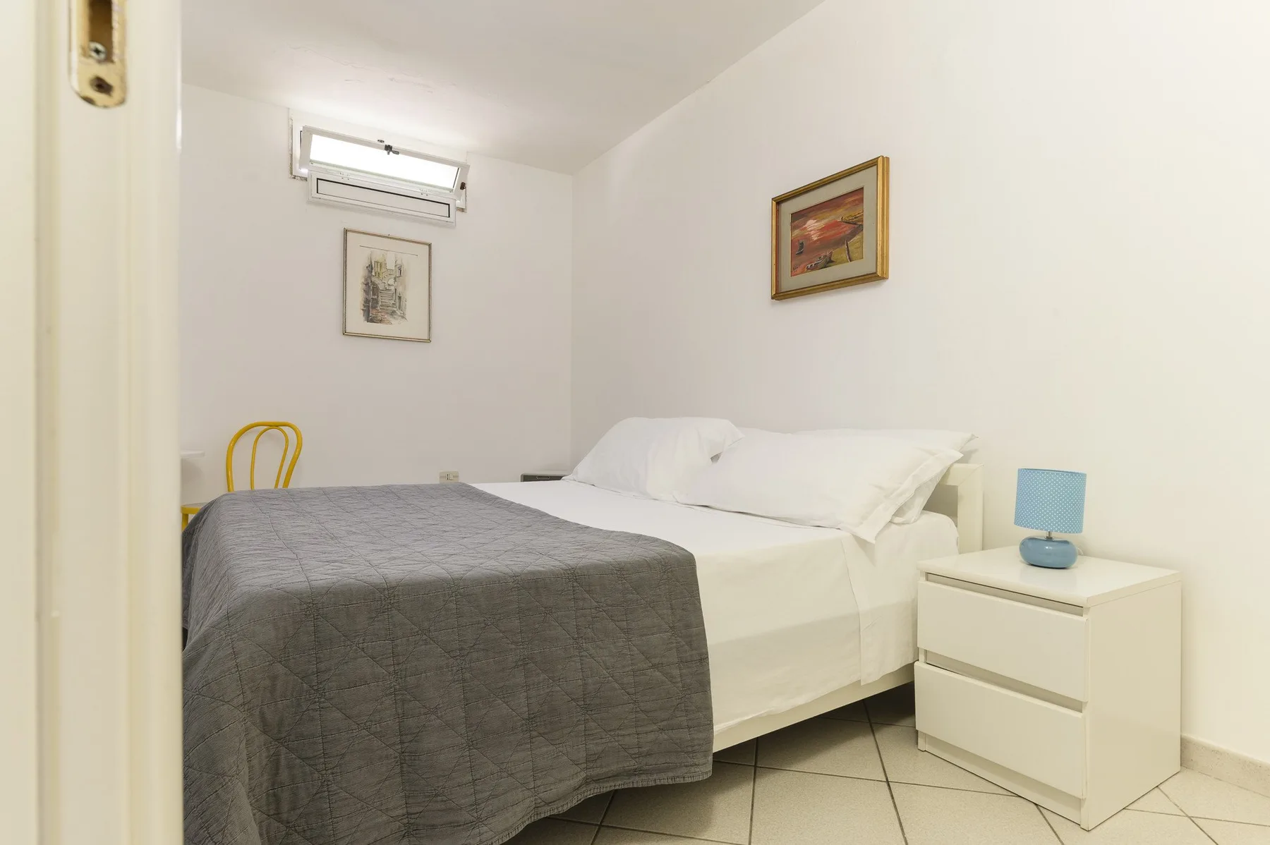 A bedroom with a bed covered by a gray blanket and a bedside table.