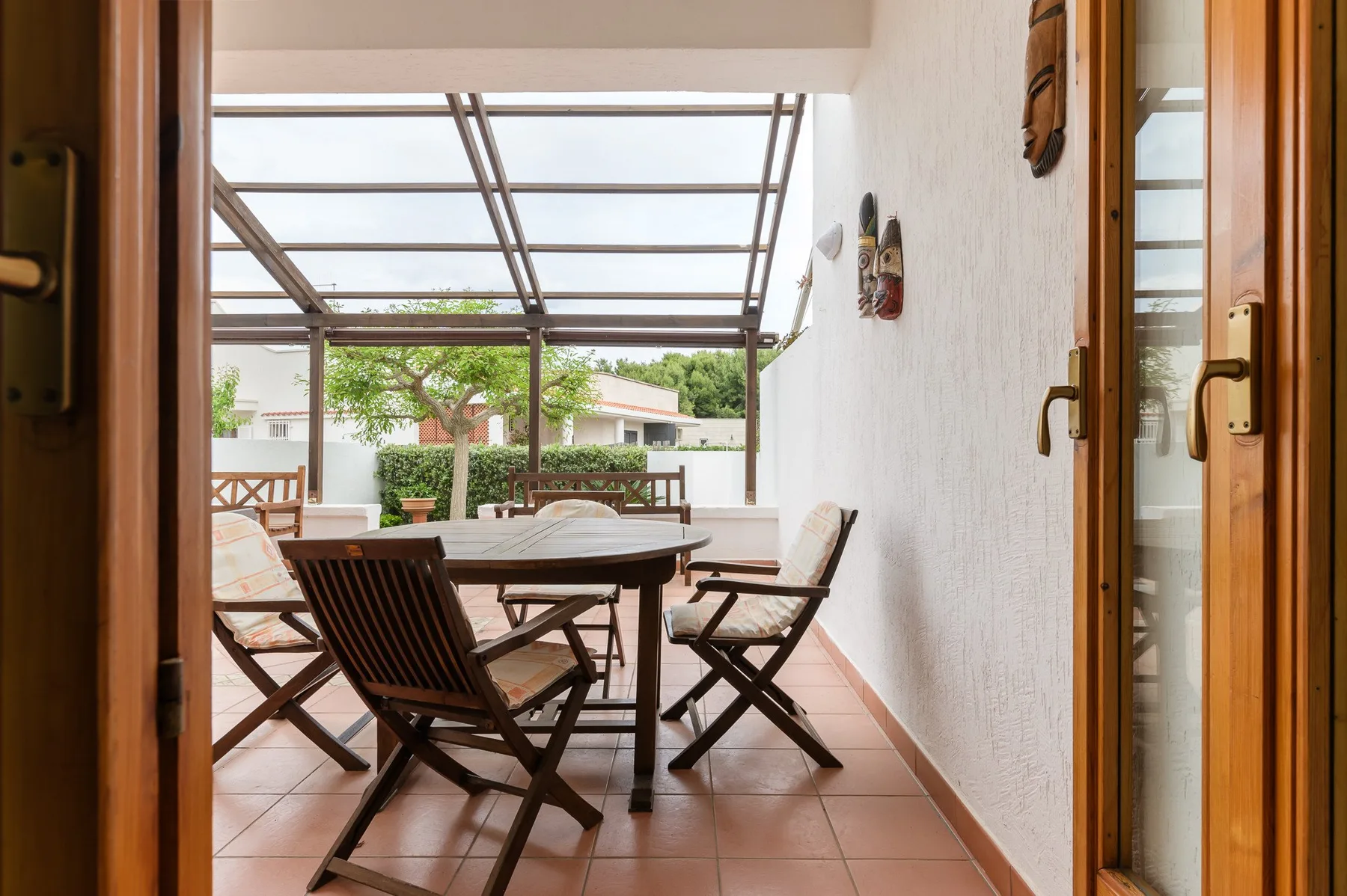 A covered patio with a dining table and seating overlooks a garden.
