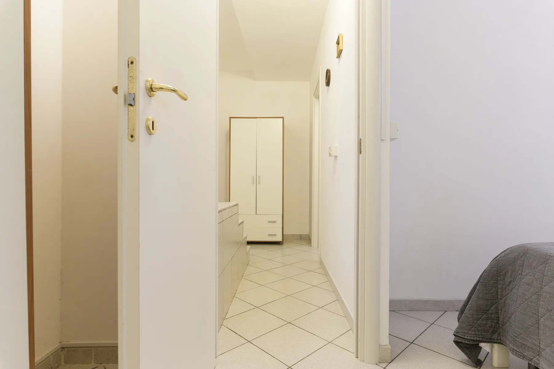A tiled hallway leads to a white wardrobe, with part of a bed visible.