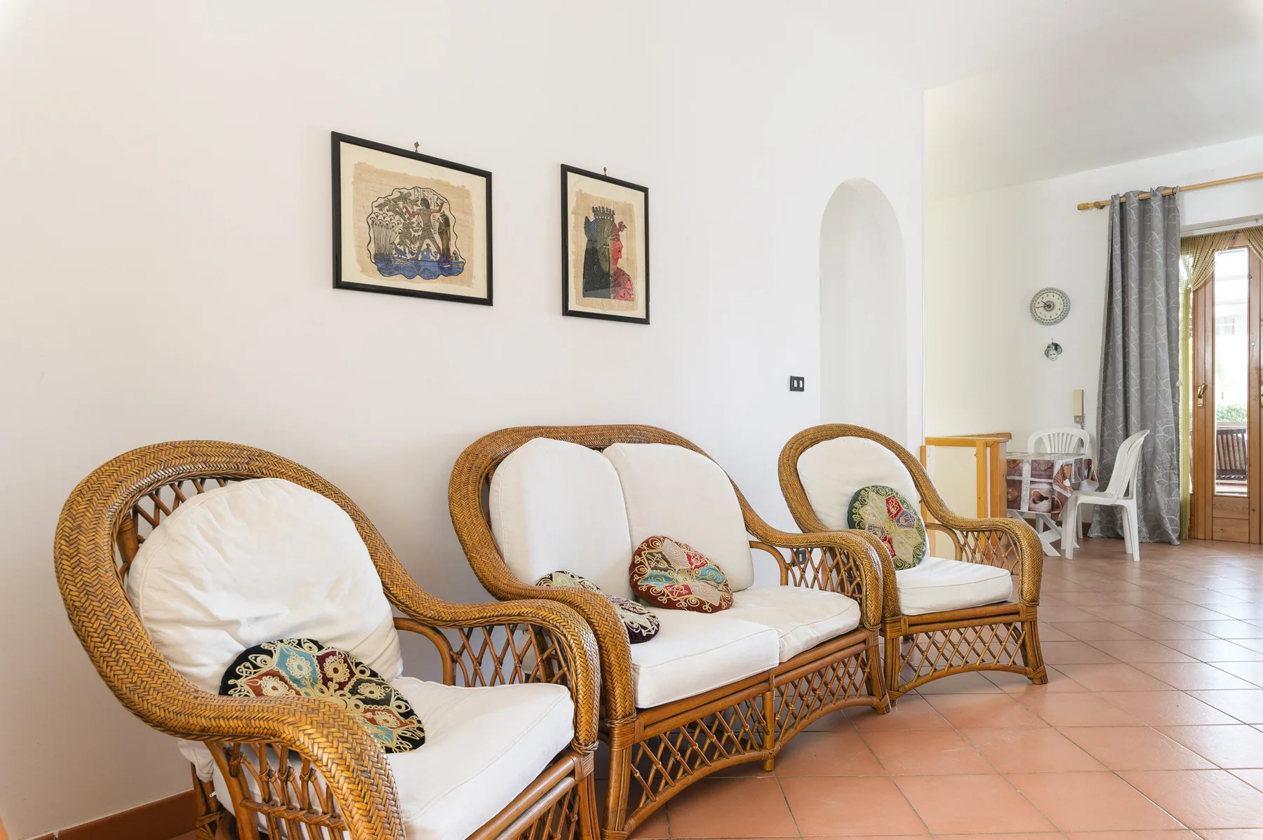 A living room with wicker seating, pale cushions, and framed pictures on the wall.