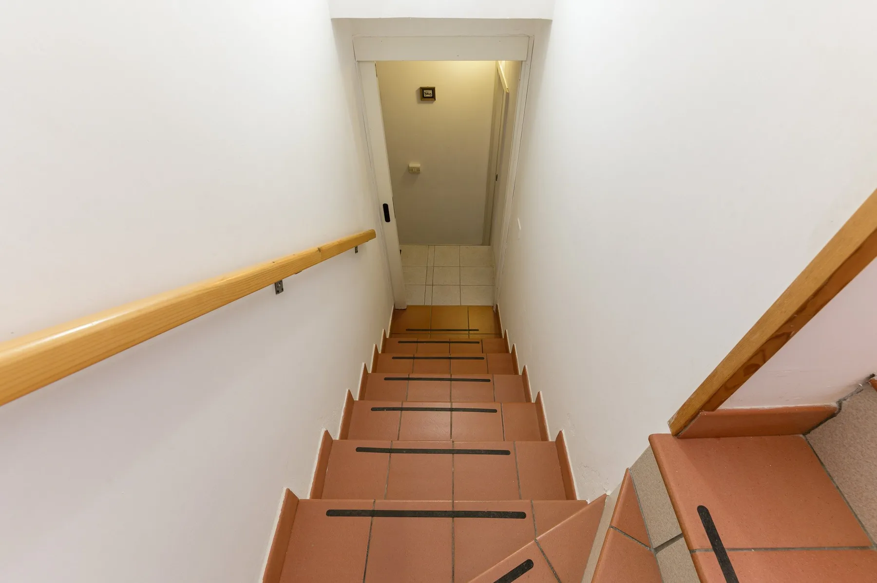 A tiled staircase descends to a small landing, with wooden handrails along the walls.