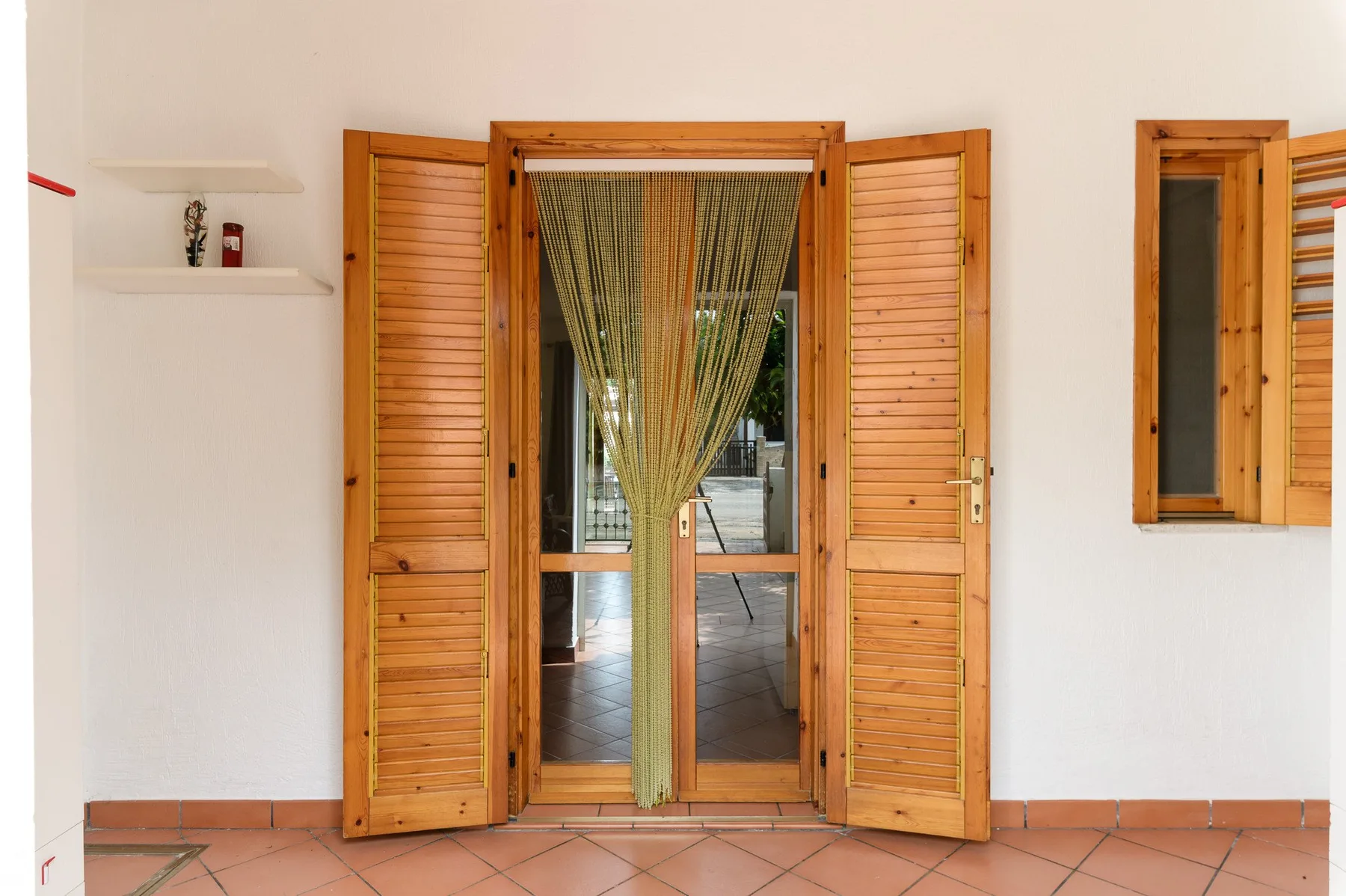 A doorway with wooden shutters and a hanging curtain opens onto a tiled interior.
