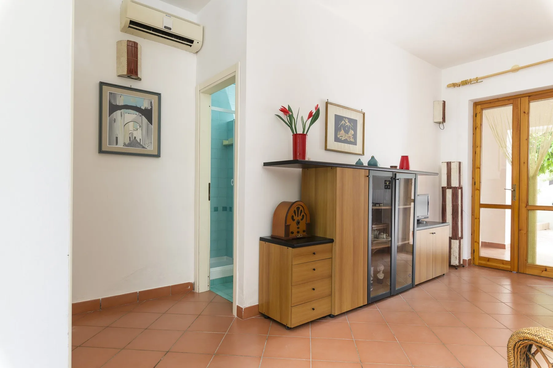 A bright living area with a wooden cabinet and glass doors opening to a balcony.