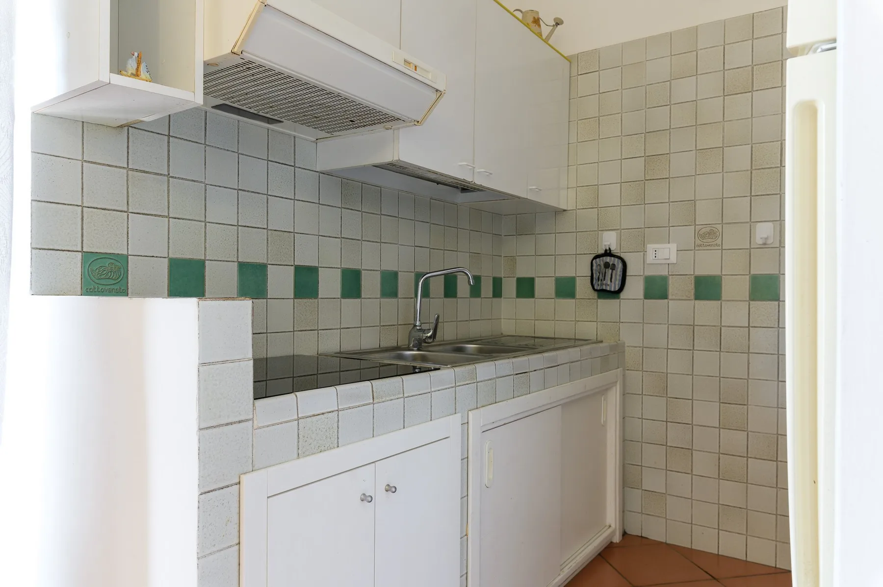 A tiled kitchen with a sink, countertop, and overhead range hood.