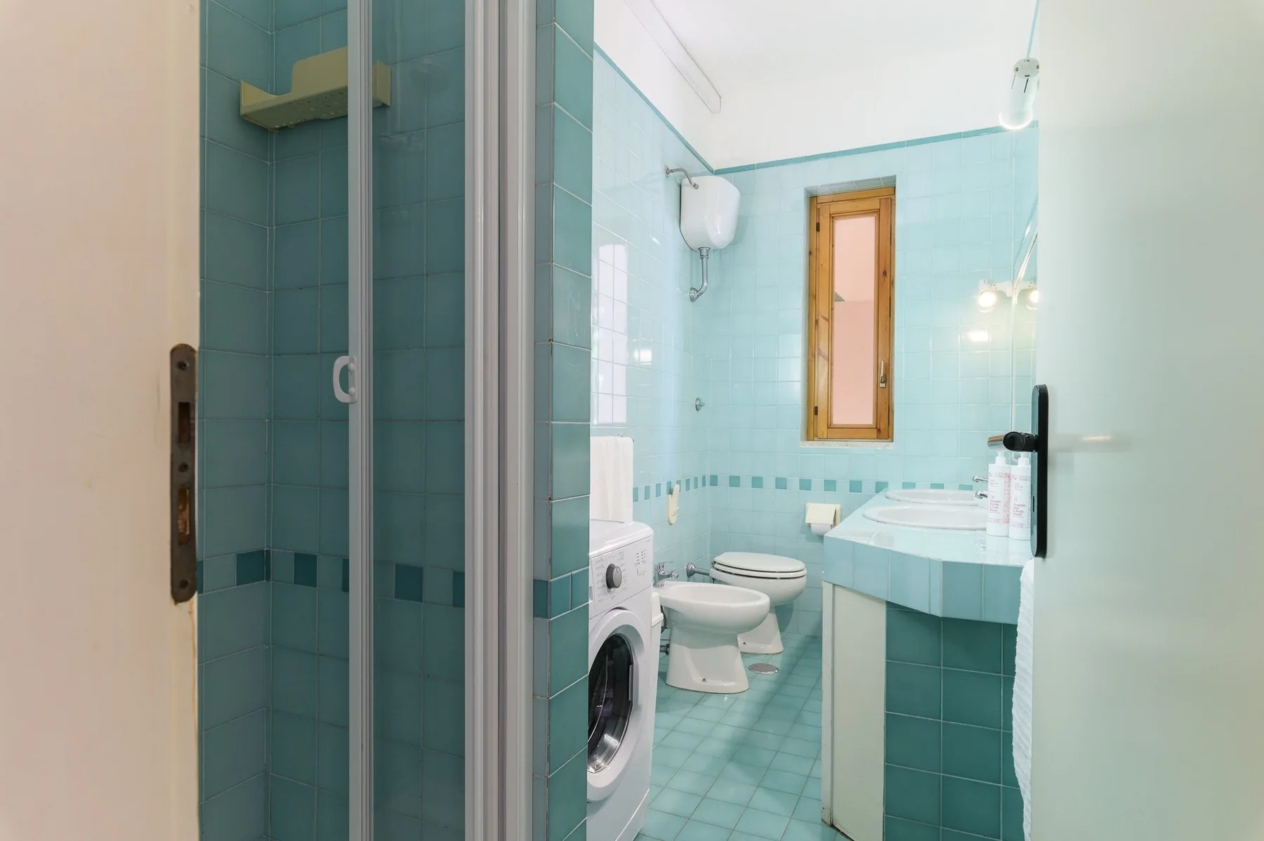 A tiled bathroom with a shower, toilet, washing machine, and sink.