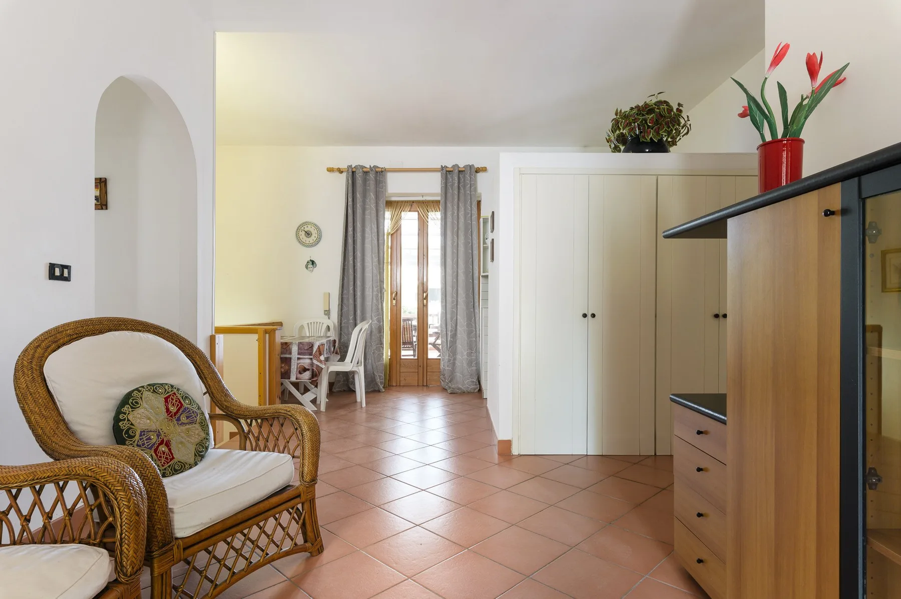 A bright room with wicker seating, a wardrobe, and glass doors opening onto a balcony.