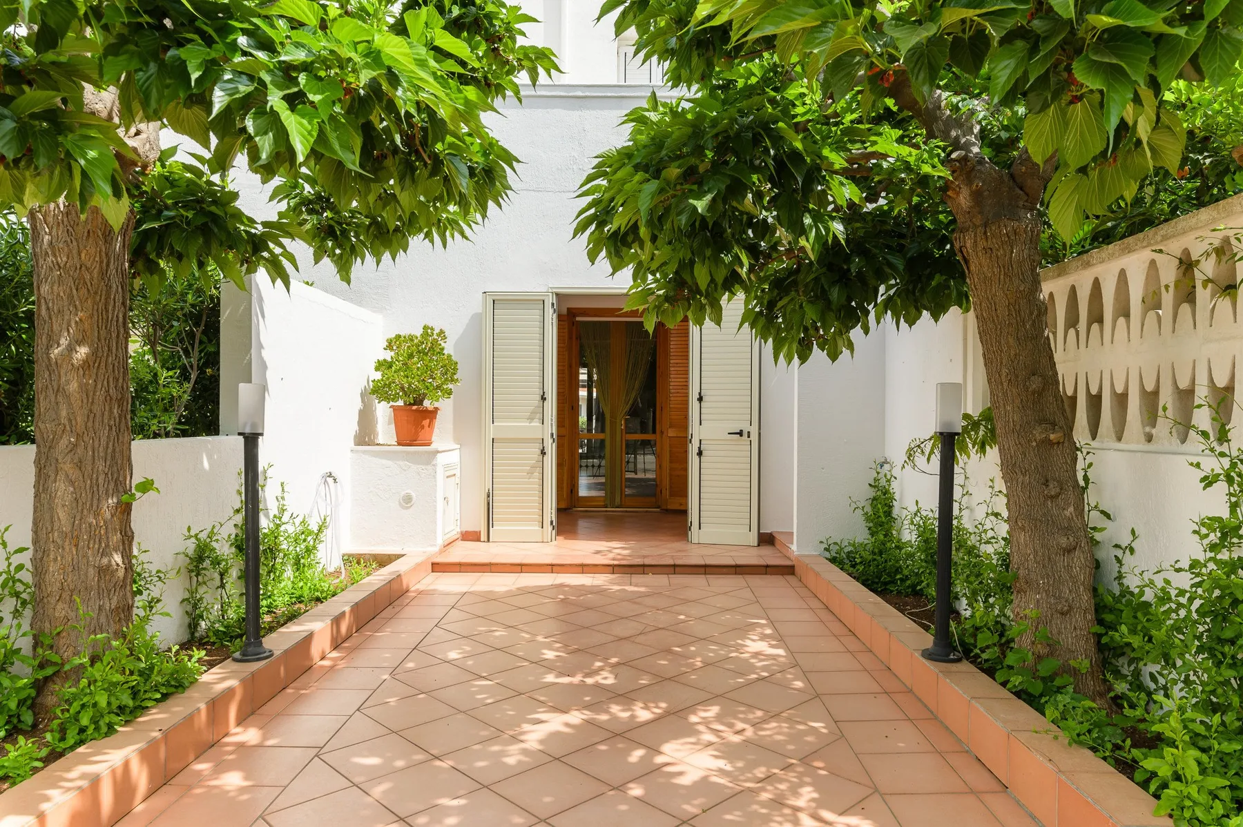 A tiled garden path leads to an open doorway beneath leafy trees.