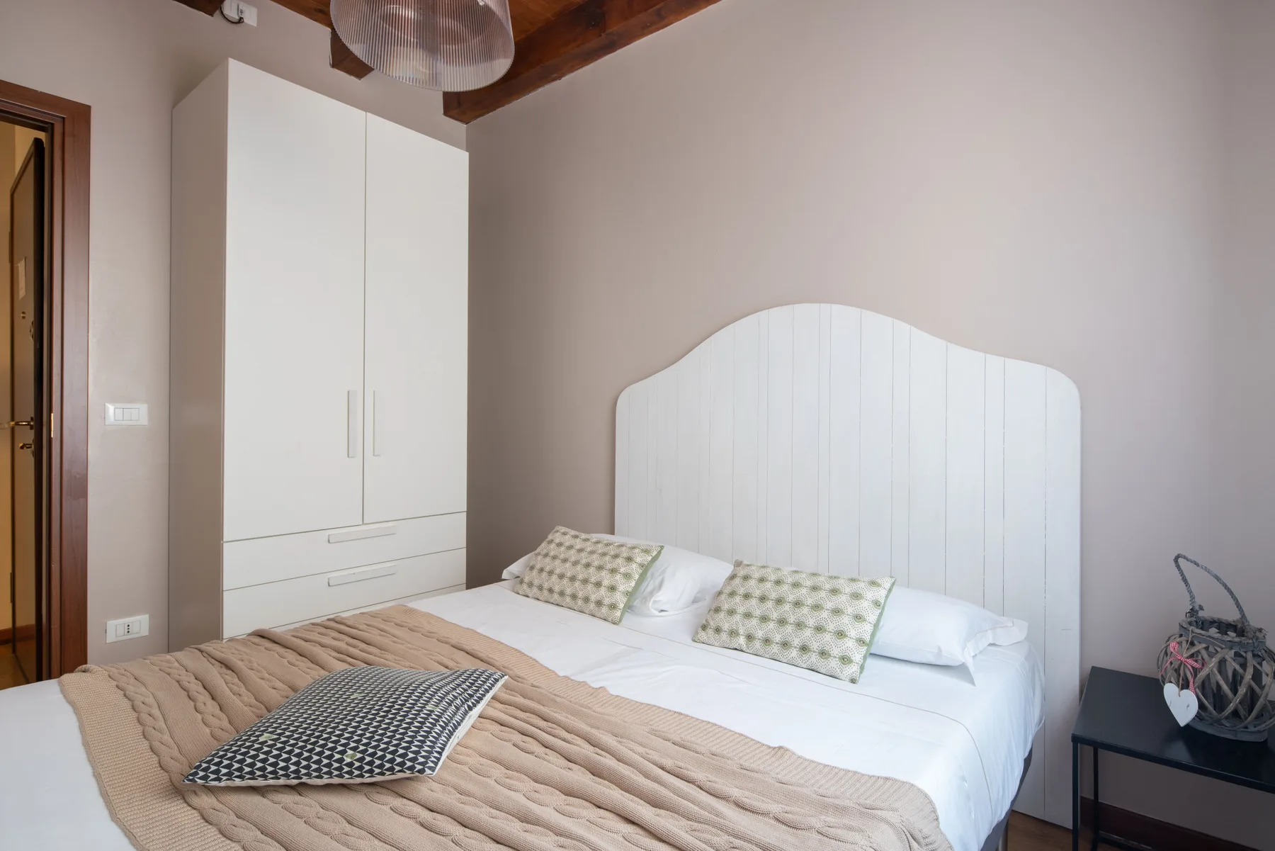 Dormitorio con una cama blanca, cojines estampados y un armario.