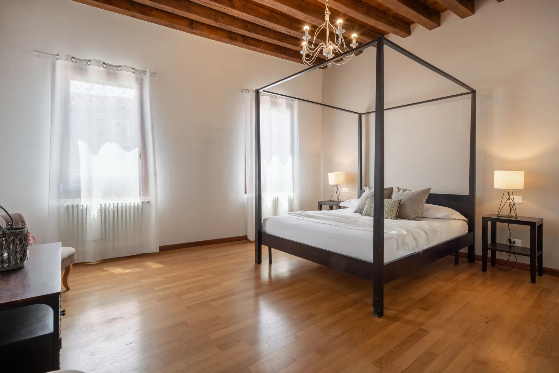 Dormitorio con cama con dosel, mesas de noche y ventanas altas con cortinas.