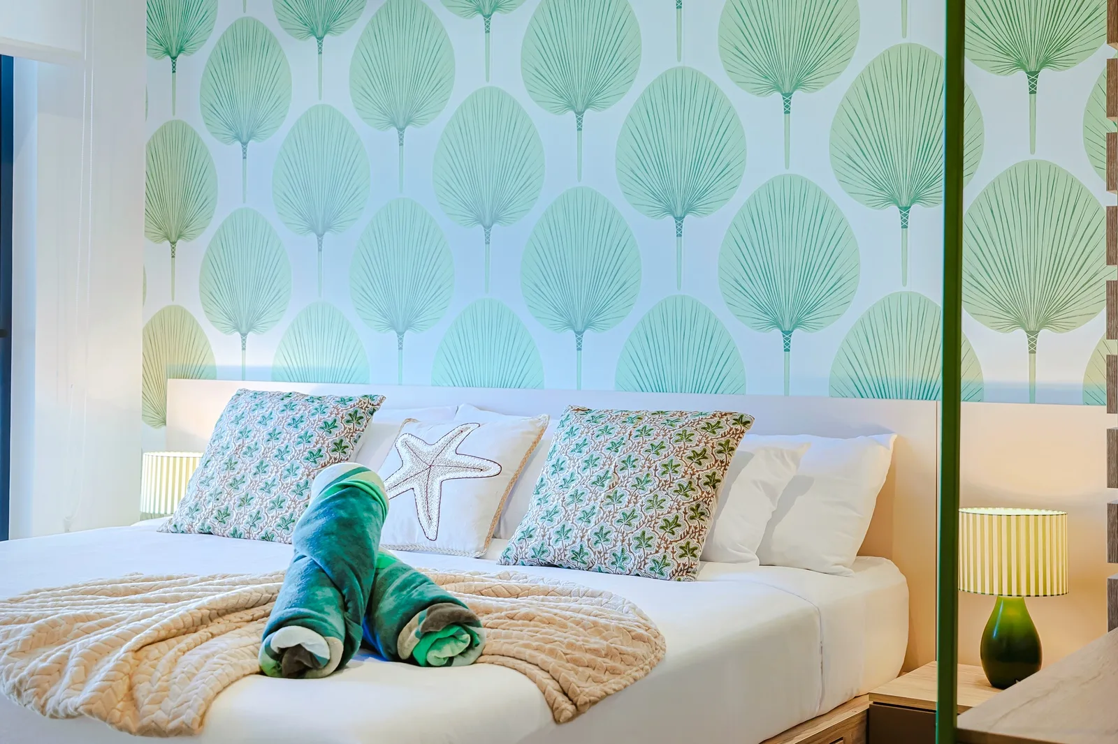 Sink into plush pillows and coastal vibes in your serene bedroom, where tropical palm-patterned walls and soft textures invite you to unwind completely.