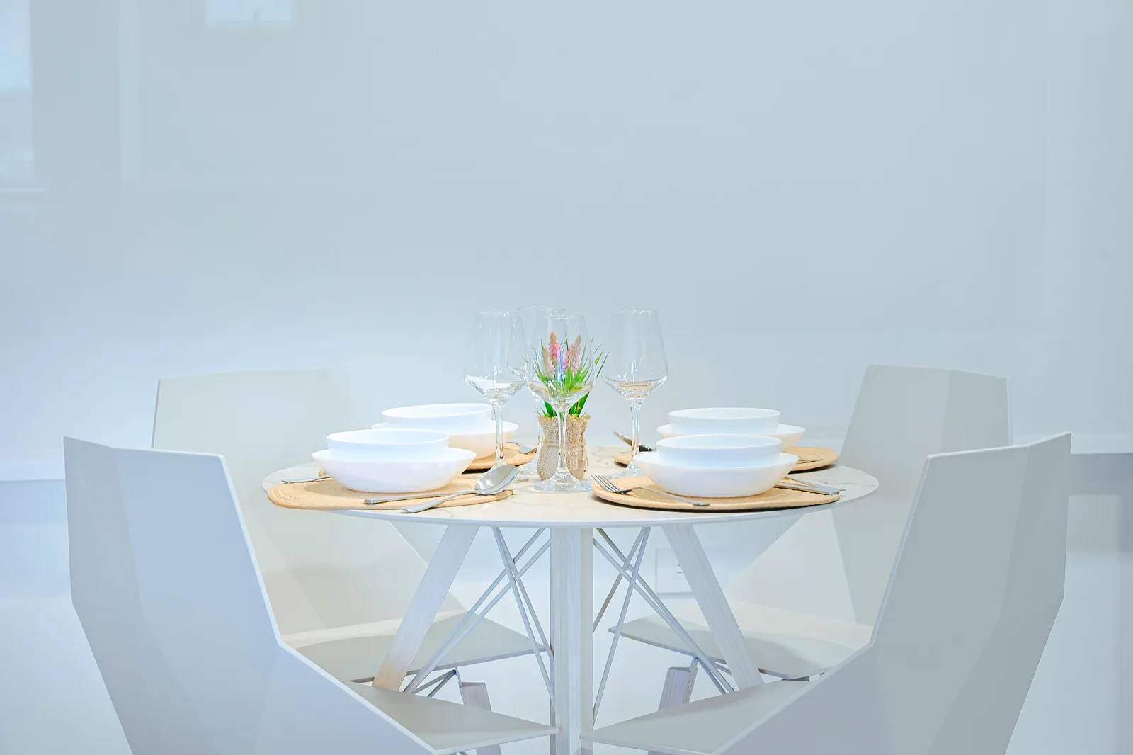 This sleek dining table is set and waiting for your meals, featuring modern white chairs, crisp white bowls, and elegant glassware