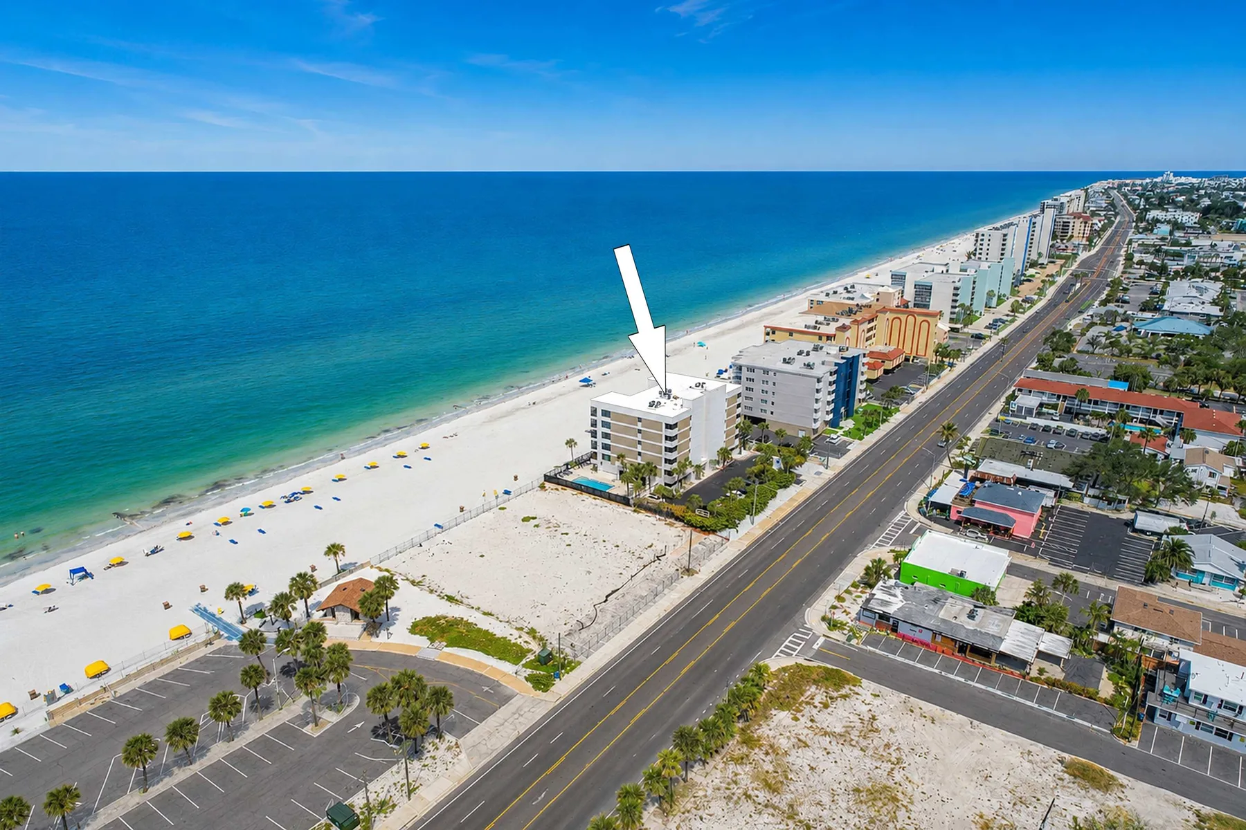 Aerial coastal scene showing a beachfront building beside the ocean and a coastal road.