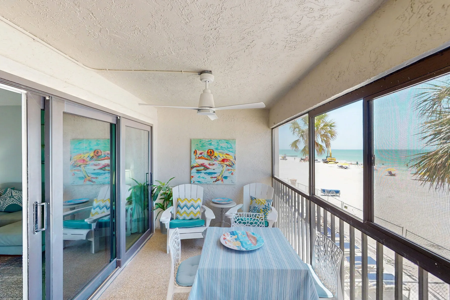 A covered balcony seating area overlooks a sandy beach and ocean.