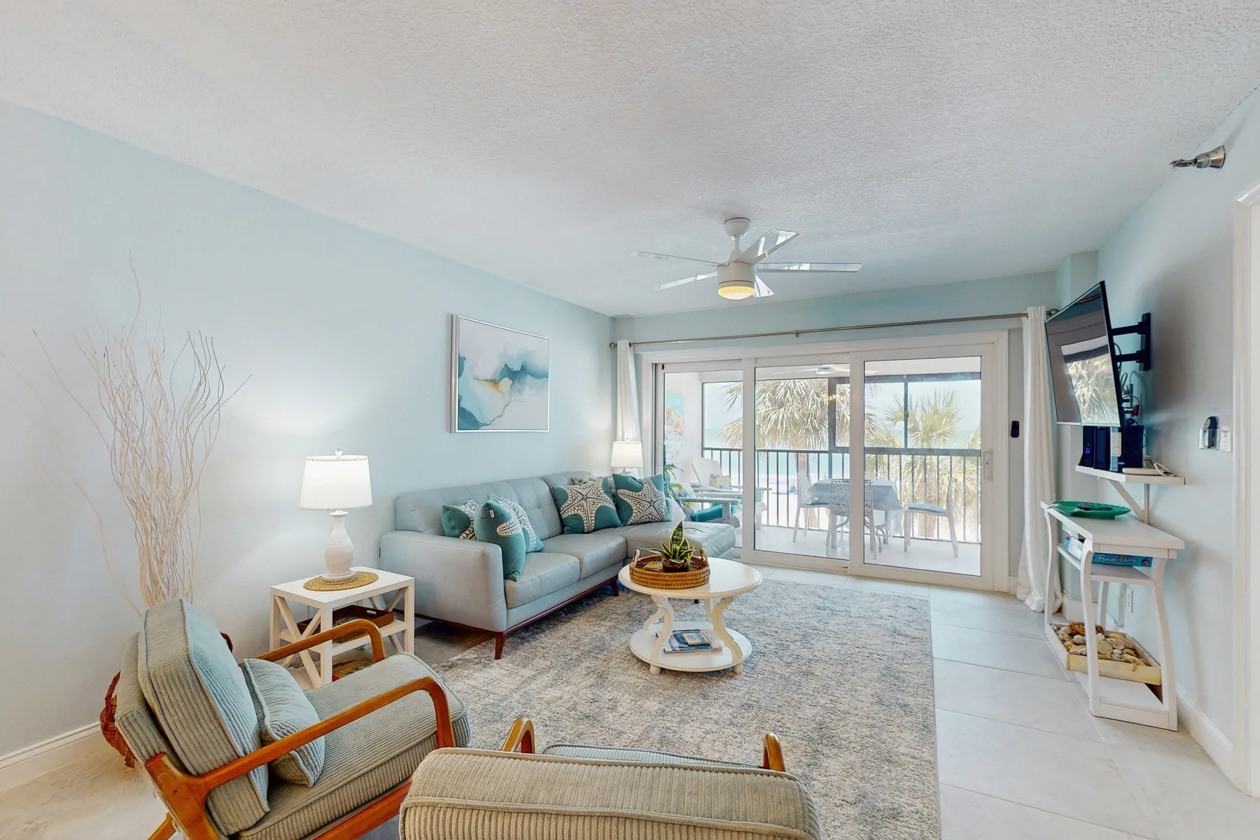 A bright living room with seating, a coffee table, and glass doors opening onto a balcony.