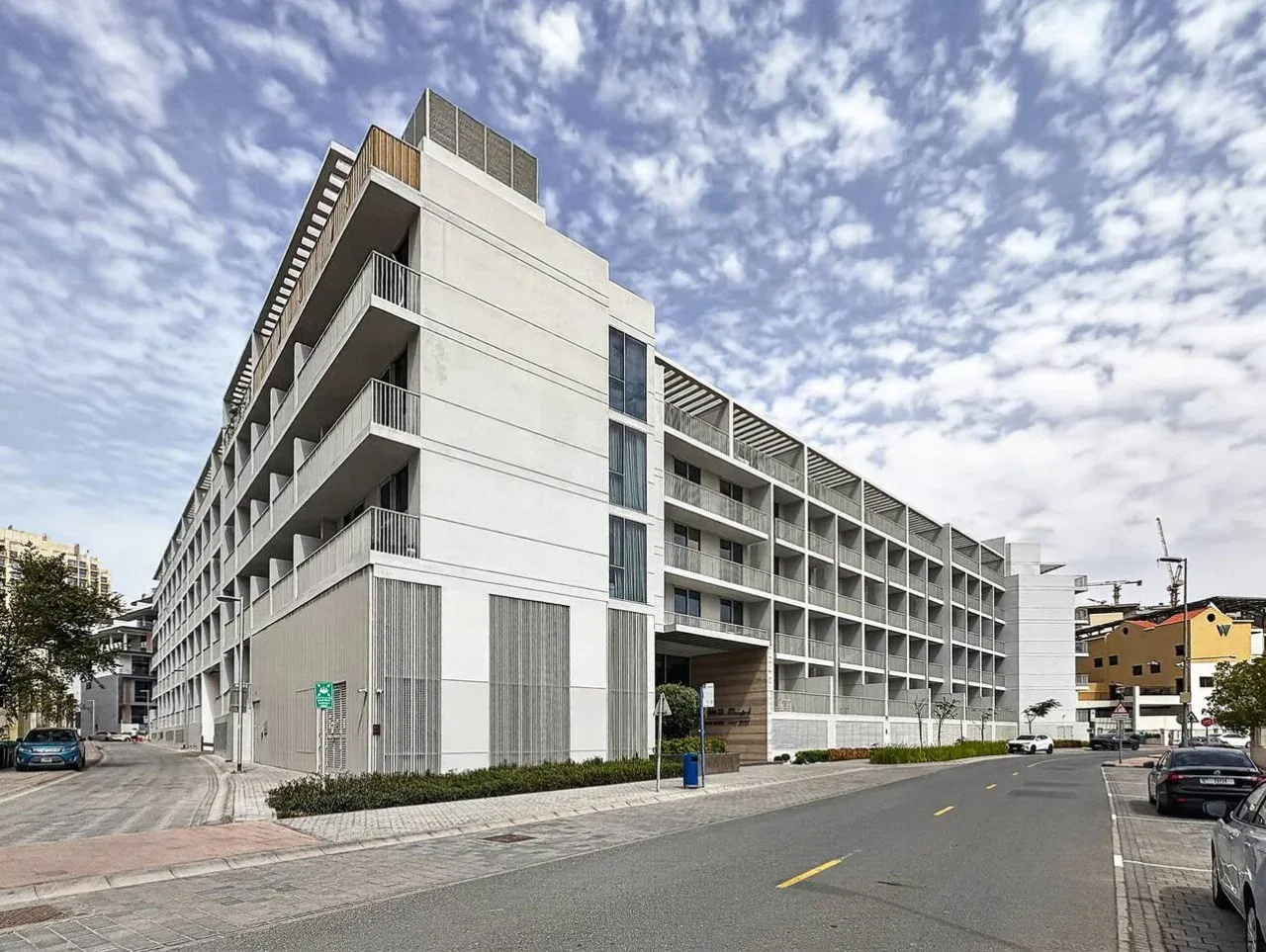 Un edificio moderno de varias plantas está junto a una calle urbana pavimentada bajo un cielo parcialmente nublado.