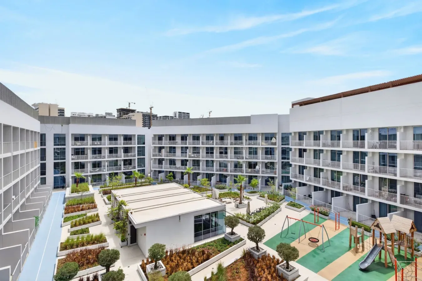 A courtyard garden sits among modern multi-story buildings, with play equipment and walkways.