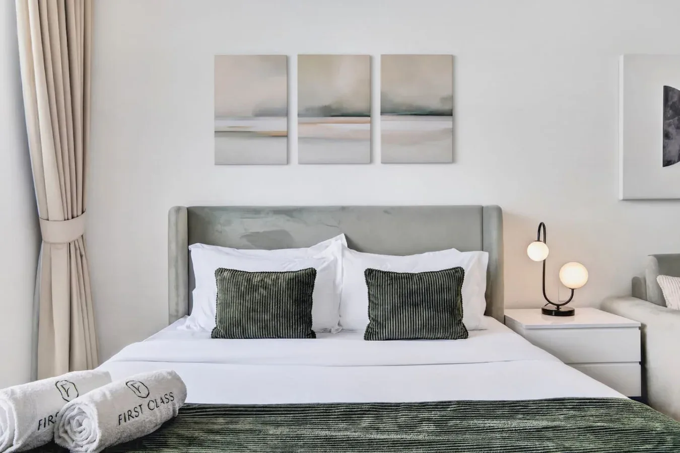 Un dormitorio con una cama bien tendida y cuadros sobre el cabecero.