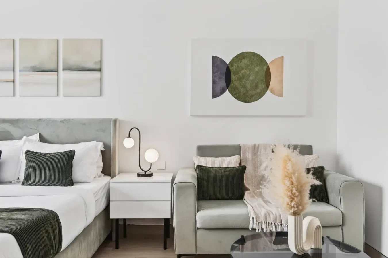 A bedroom with a neatly made bed and an upholstered armchair beside a small table.