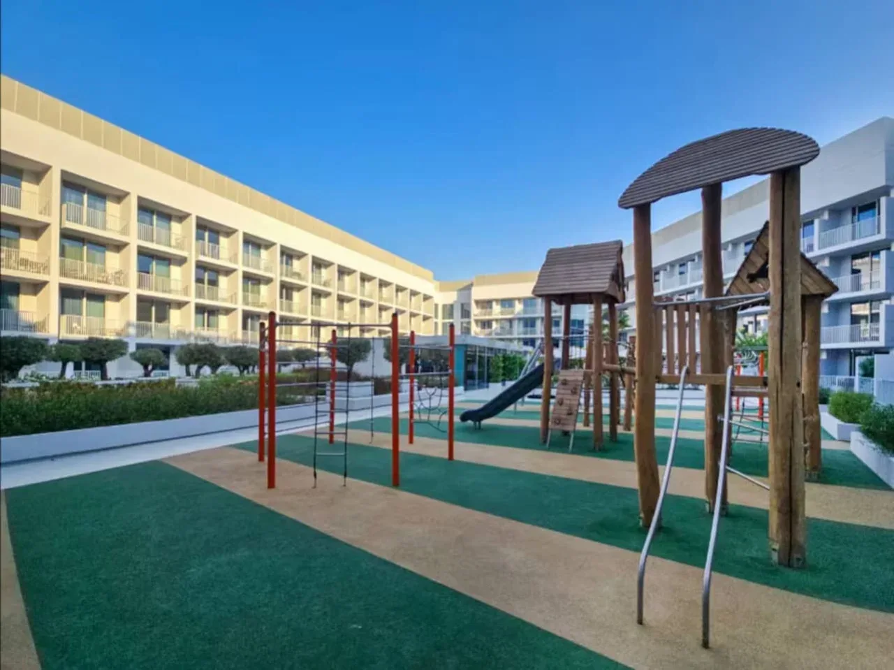 Un parque infantil al aire libre con estructuras para trepar y columpios se encuentra entre edificios de apartamentos.