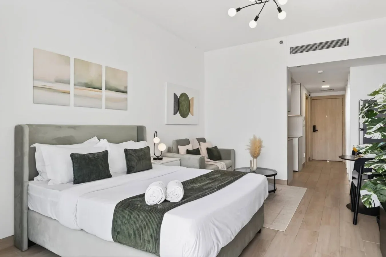 Un dormitorio tipo estudio luminoso con una cama bien tendida y una pequeña zona de estar.