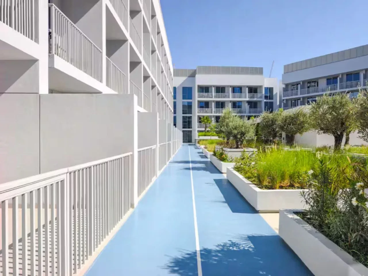 Un sendero azul al aire libre pasa entre edificios modernos y jardineras elevadas.