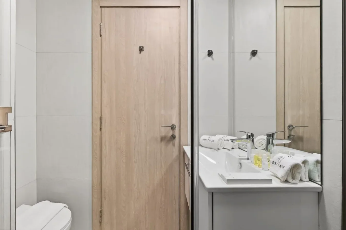 Un baño alicatado con lavabo y espejo junto a una puerta de madera.