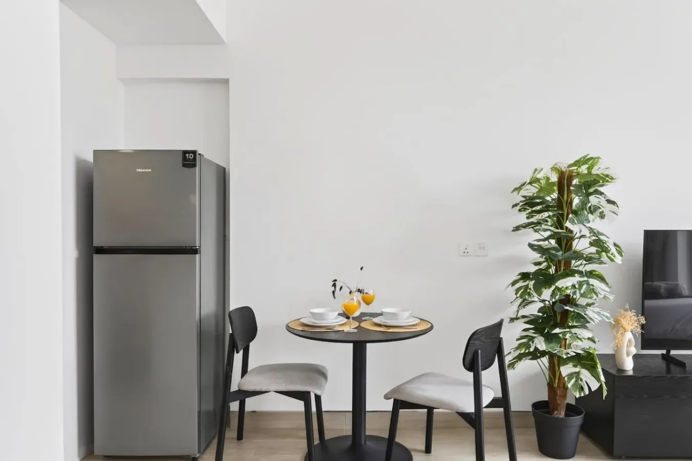 Comedor con una mesa redonda y sillas junto a un refrigerador y una planta en maceta.