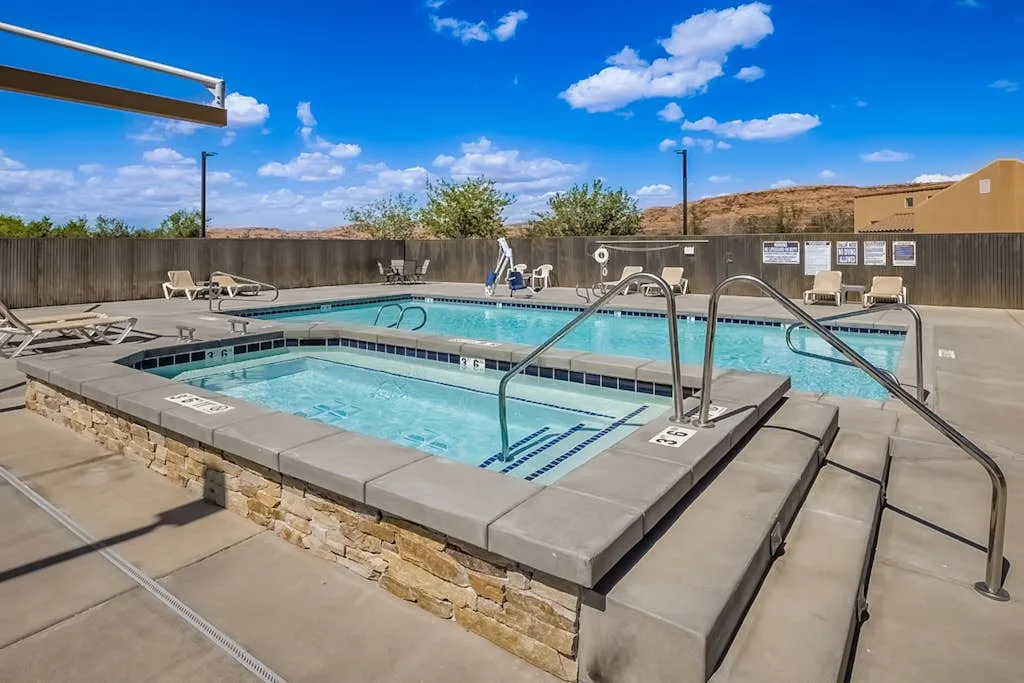 Una piscina al aire libre con una piscina más pequeña contigua y pasamanos metálicos.