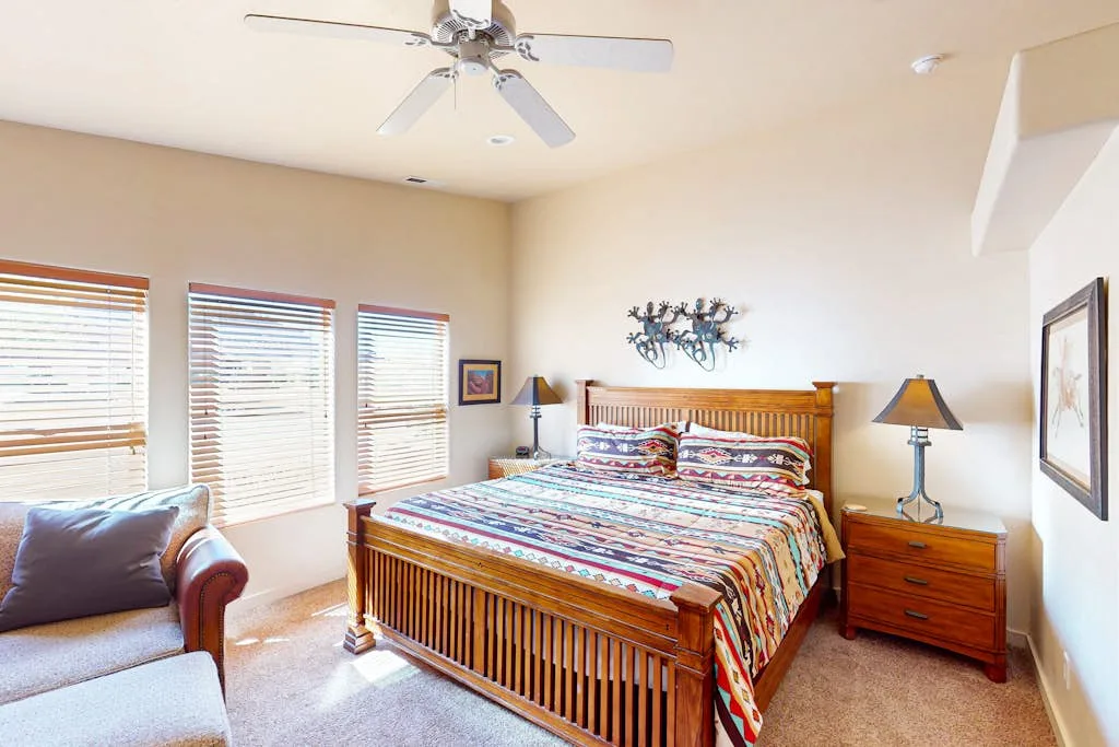 A bedroom with a wooden bed, patterned bedding, and windows with blinds.