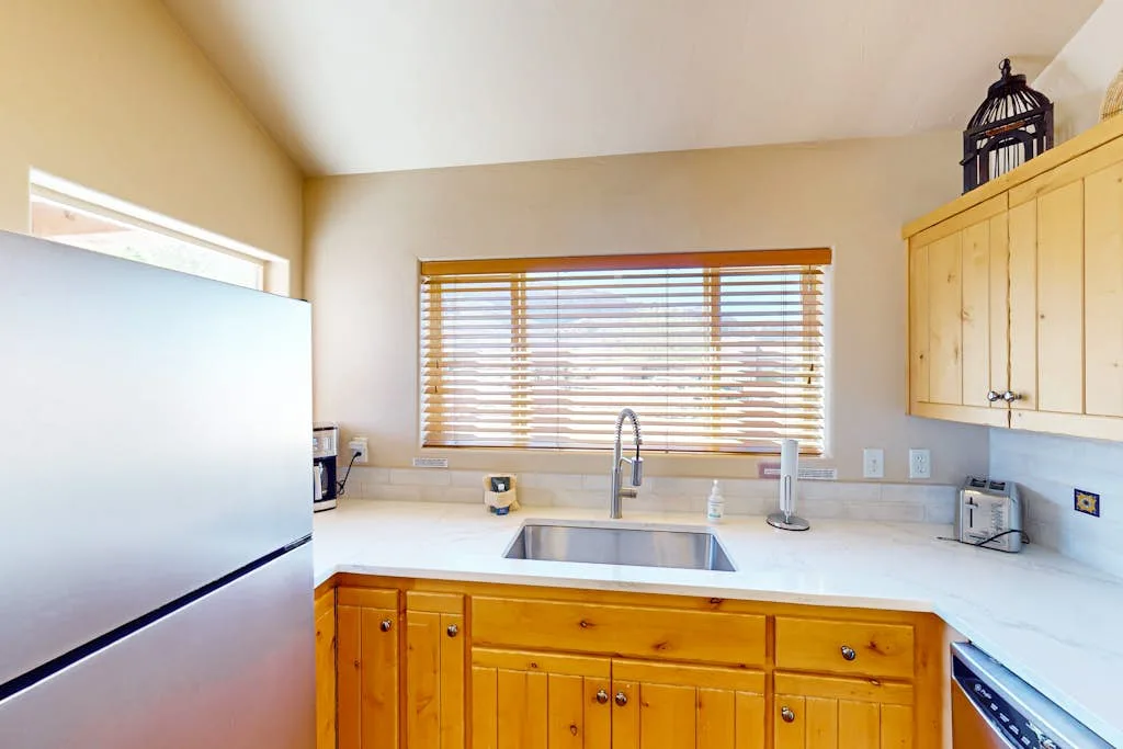 A bright kitchen with wooden cabinets, a sink, and a window with blinds.