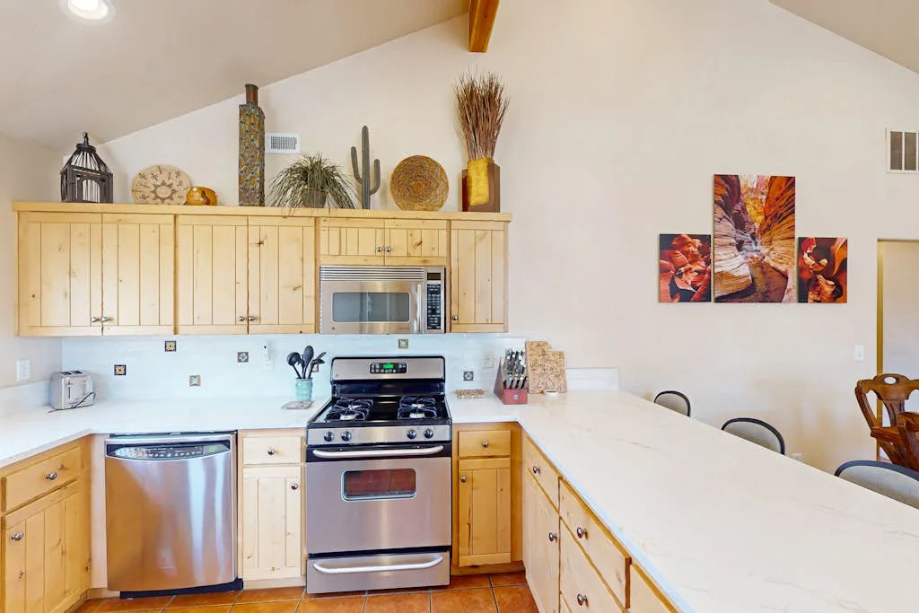 A bright kitchen with light wood cabinets, a stainless-steel stove, and a long countertop.