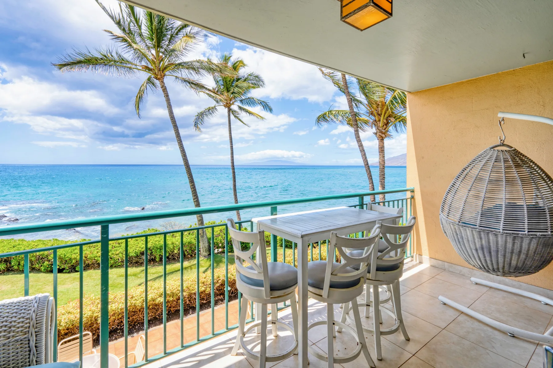 A covered balcony overlooks the ocean, with a dining table and hanging chair.