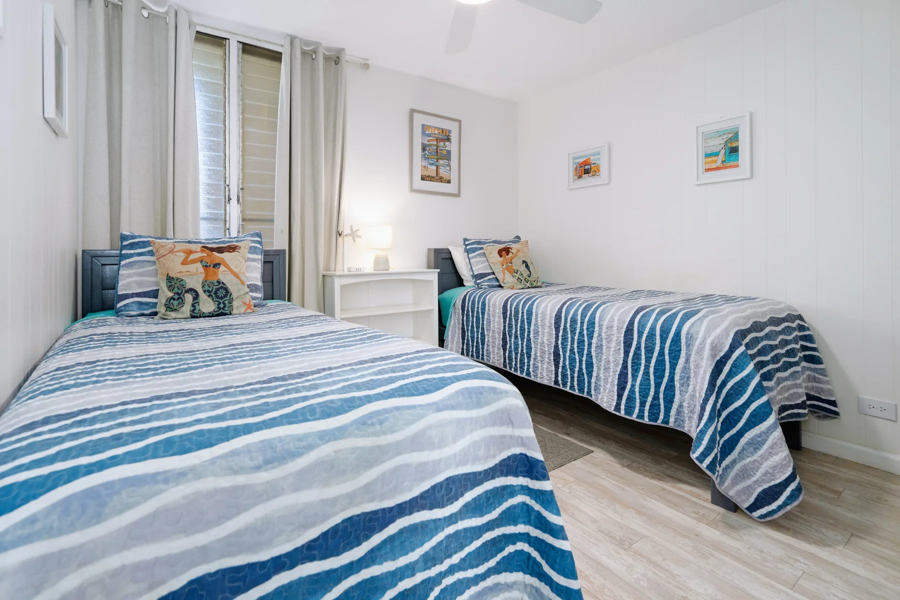 A bright bedroom with two beds covered in blue and white striped bedding.