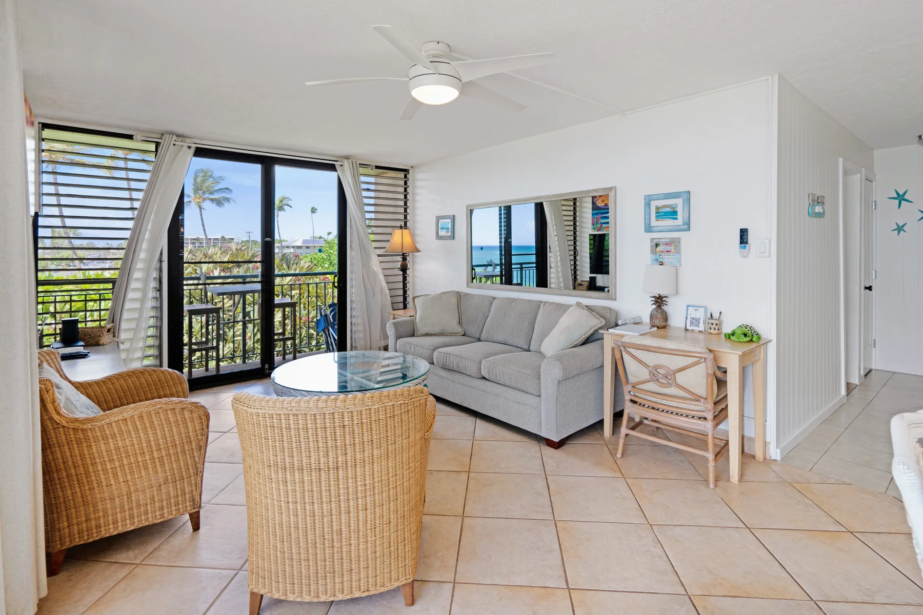 A bright living room with wicker seating, a gray sofa, and balcony doors.